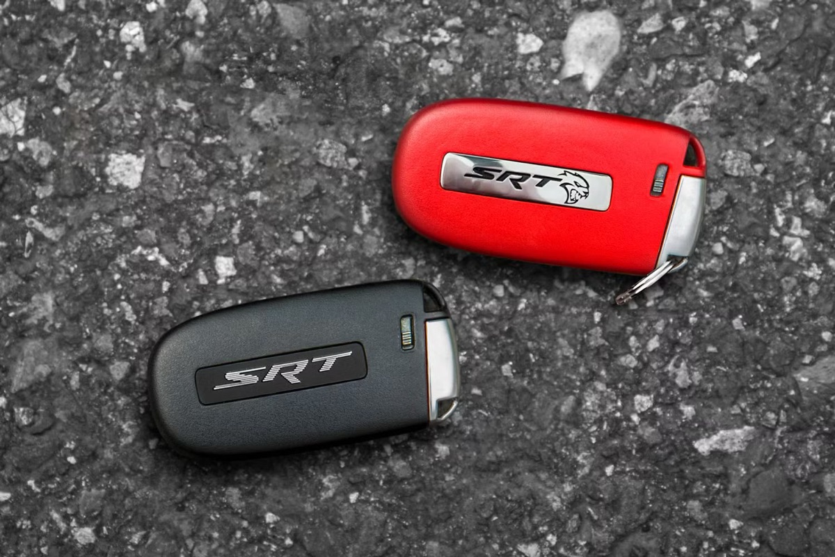 Two Dodge SRT Hellcat key fobs on asphalt: a red one and a black one.